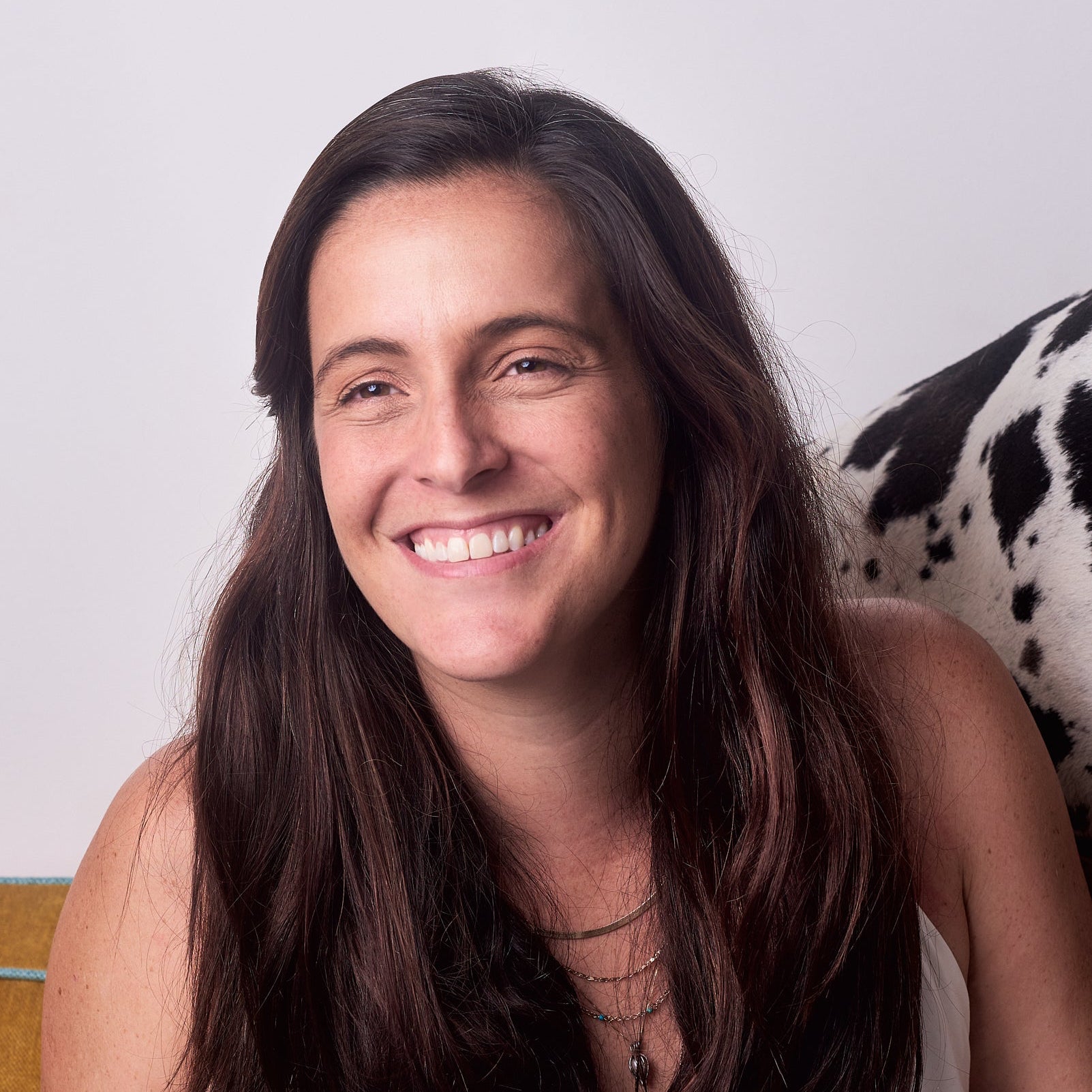 Woman with long dark hair wearing a white top sitting on a patterned chair.