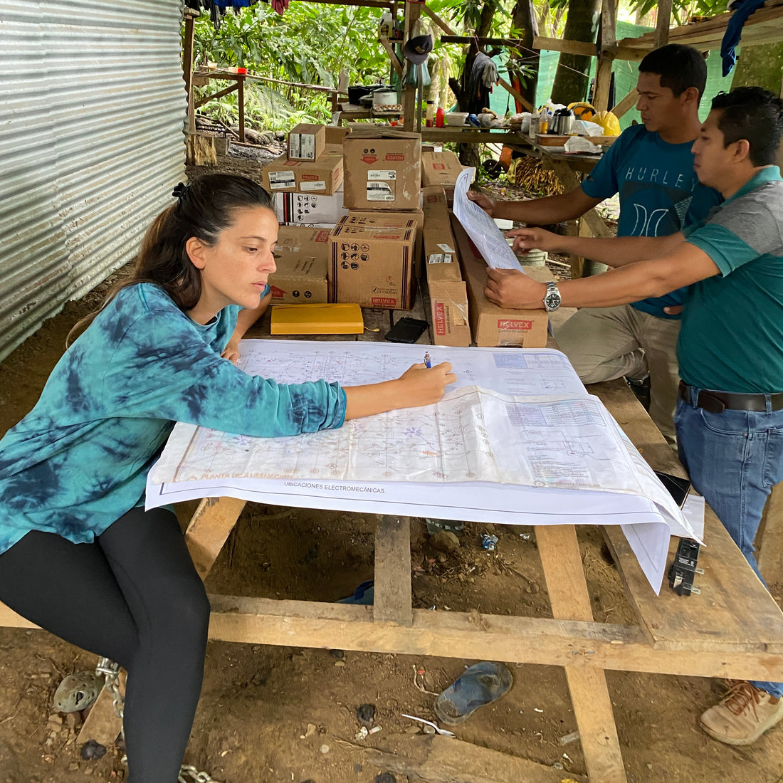 Two people working on blueprints in a rustic setting with wooden structures and tools.